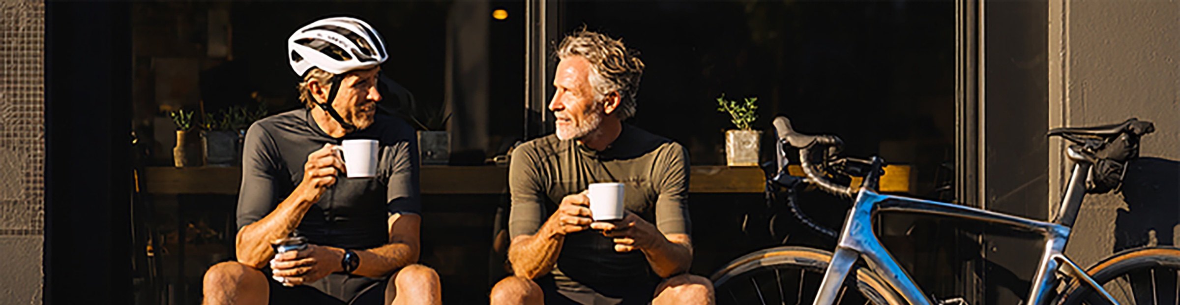 Two cyclists talking over coffee with a road bike parked beside them.